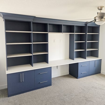 Home office in a deep blue matte finish with white shelves and traditional crown molding.