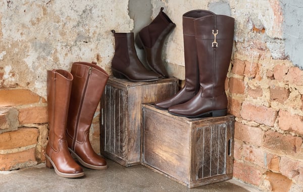 Three pairs of boots are displayed on wooden boxes in front of a brick wall.