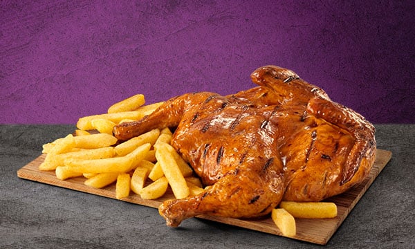 Steers® Full Chicken with a portion of chips on a wooden board placed on a grey surface with a grey background.