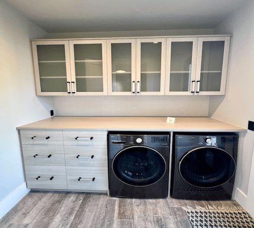 Custom laundry room with washer/dryer, sink and light grey wood cabinets and shelves. Home in Sylvan Lake.