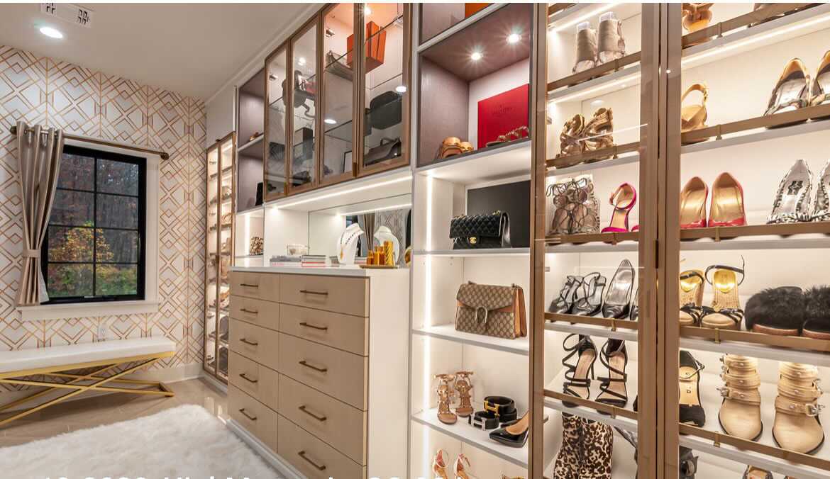 luxe walk in closet with lighting and glass doors, accenting shoes and hand bags