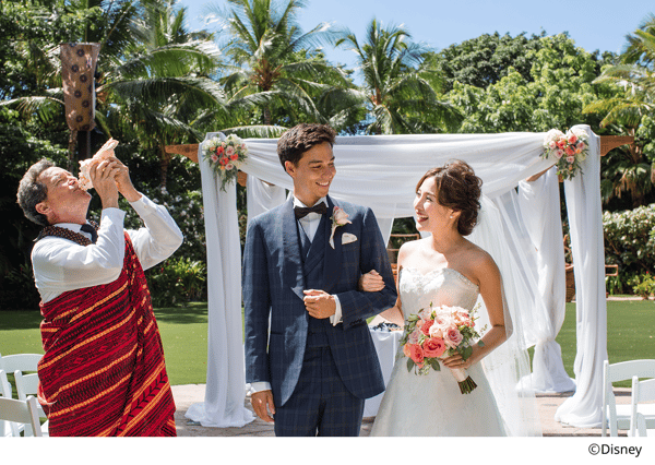 挙式会場で見つめあう新郎新婦と楽器を奏でる男性