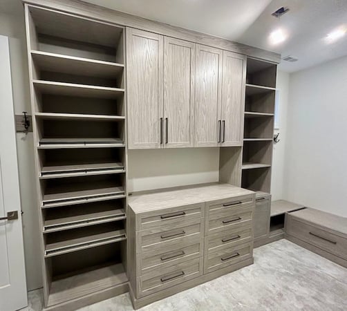 Light wood walk-in closet with custom shoe storage, built-in cabinets, drawers, shelving, and bench seating for home organization