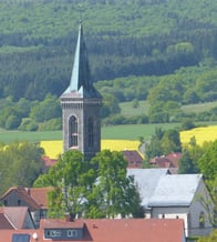 Das Bild zeigt die 
Evangelische Kirche Crainfeld aus der Distanz. Der spitz Kirchturm ragt aus dem Dorf raus