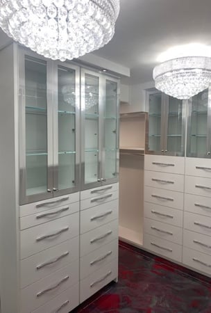 White walk-in closet master closet with aluminum framed glass doors and custom handles on multiple banks of drawers