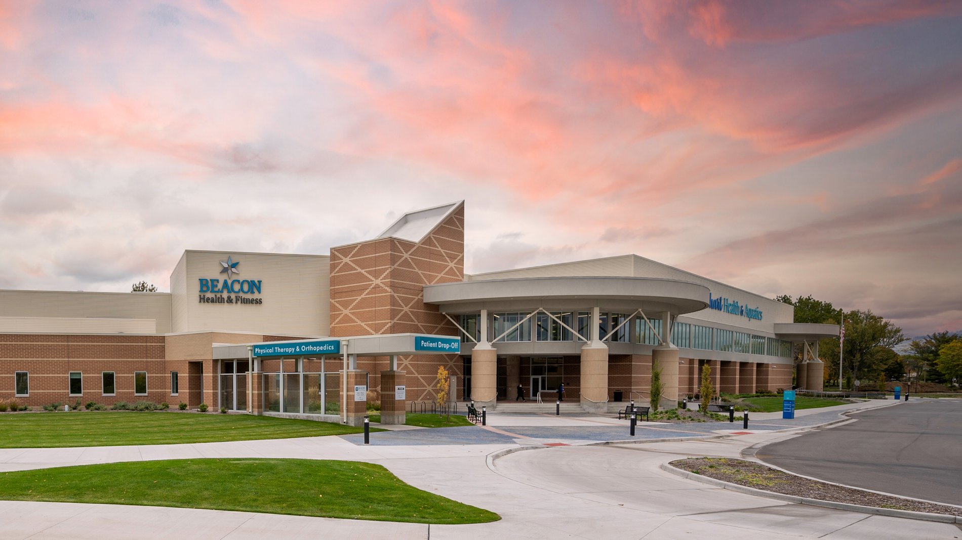The modern, tan building of Beacon Health & Fitness in Elkhart. It has signage that indicates areas for aquatics, patient drop-off, and physical therapy and orthopedics.