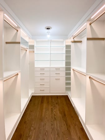 Walk in closet in a white finish with lighting and gold hardware.