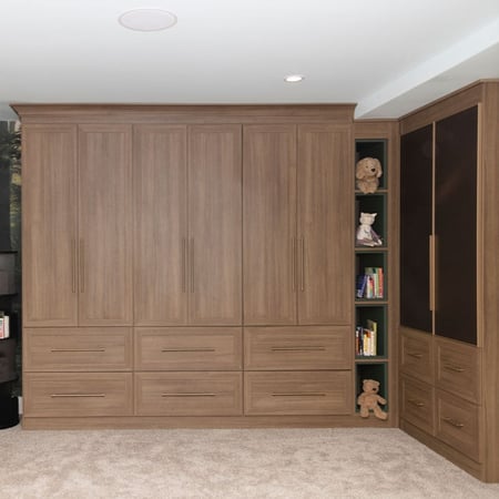 A playroom designed in a wood grain finish with dark green shelves, glass doors, and gold hardware.