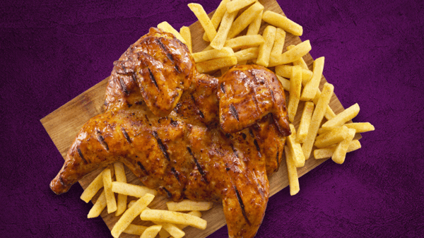 Flame-Grilled full chicken with chips on a brown board.
