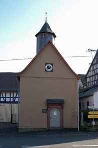 Das Bild zeigt die Evangelische Kirche Feldatal-Zeilbach von außen. Die Kirche fällt durch den spitzen Turm und einer Uhr auf.