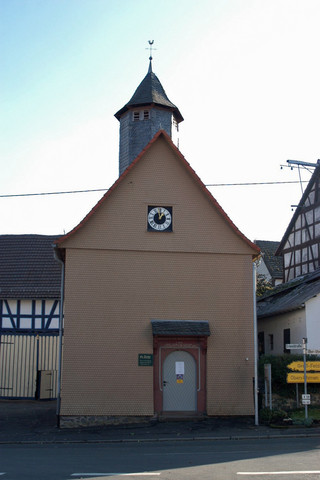 Das Bild zeigt die Evangelische Kirche Feldatal-Zeilbach von außen. Die Kirche fällt durch den spitzen Turm und einer Uhr auf.