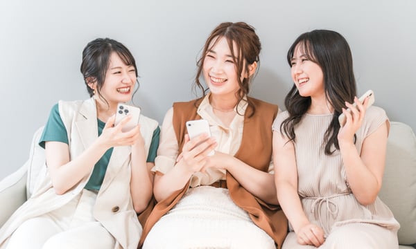 スマホをもって微笑む３人の女性