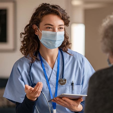 A woman wearing medical scrubs and a mask holding a tablet