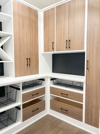 A warm and welcoming walk-in pantry designed in white with brown and black accents. Complete with hidden storage, wine storage, wide set drawers, and baskets.