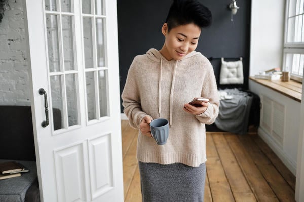 Woman holding a cup of coffee in one hand and her mobile phone in the other.