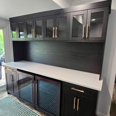 Custom home bar with black cabinetry, glass-front cabinets, and white countertop.