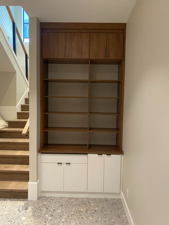 Custom bookshelf and storage system with mixed colors and finishes. This system has upper and lower closed cabinetry and open shelving in the middle.