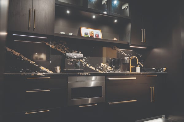 Custom coffee bar cabinetry featuring Shadow Black cabinets, under-cabinet lighting, a coffee station, stone backsplash, and built-in storage.