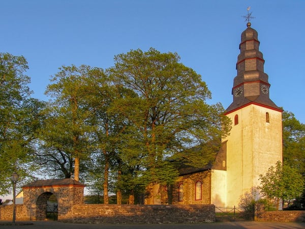 Inmitten eines schön gepflegten Kirchplatzes steht seit 300 Jahren unsere Kirche. 1716 erbaut ist sie ein heller schöner Barockbau mit einer sehr guten Akustik. Schon im 12. Jahrhundert ist hier eine Kirche beschrieben. Der Kirchenturm ist weit über die Grenzen des Westerwaldes bekannt, denn er hat eine dreifach gegliederte Barockhaube. Eine 1614 gegossene Glocke klingt noch heute. Die 1725 vom Orgelbauer Florenz Wang erbaute Orgel fügt sich gut in das helle und freundliche Ambiente ein.
