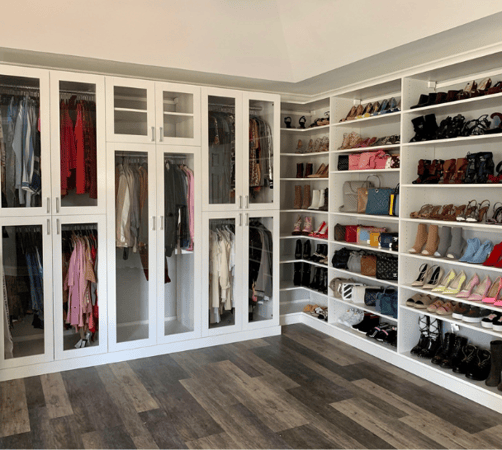 Img 4 California Closets Orange County NY White Walk-in Closet with Clear Glass Doors, Variety of Hanging Heights for Wardrobe, and Angled Shoe Shelving, Full Shoe Wall