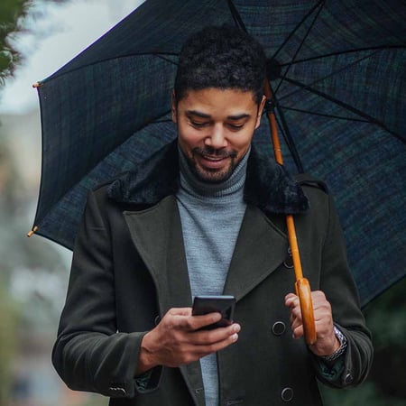 Man holding an umbrella with his left hand and looking at a smartphone in his right hand