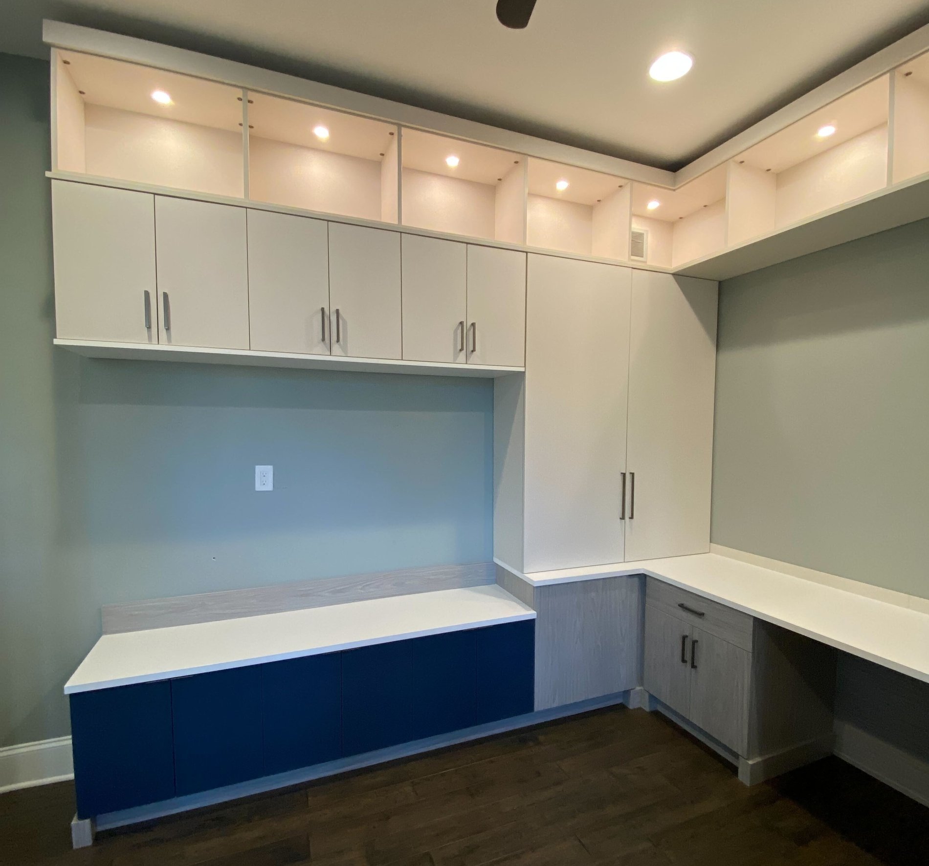 Custom desk with upper and lower cabinets, lighting, and silver hardware. has accent blue doors for the bottom section