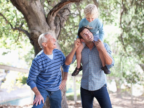 Smiling grandfather looking at son while grandson is on his shoulders