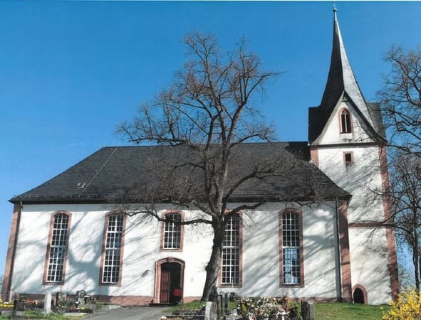 Auf einer über dem Dorf gelegenen Basaltkuppe steht weithin sichtbar die von einem ummauerten Kirchhof umgebene Kirche.
Der Turm gehört noch in die erste Hälfte des 13. Jahrhunderts, während die vier massiven Dreiecksgiebel mit spätgotischen Maßwerkfenstern und der achtseitige, leicht konkav geschweifte Spitzhelm in einer späteren Umbauphase entstanden sind.