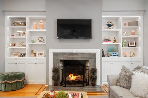 fireplace with TV above and white built-in cabinets on each side with couch and ottoman