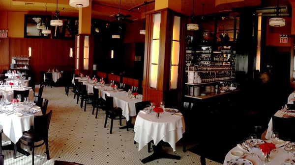 The elegant dining room of Paola's Restaurant in New York City with each table covered in a white tablecloth with a small bouquet of red roses on each table.