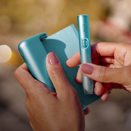 Female hand holding a light blue IQOS ILUMA i PRIME pocket charger and holder