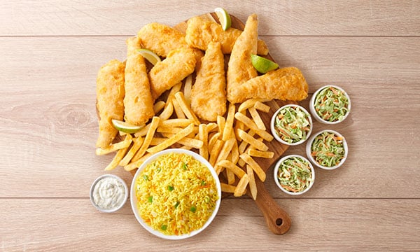 Four baby hakes with chips on a wooden board placed next to a bowl of rice, coleslaw and sauce.