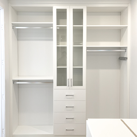 California Closets walk-in closet designed in a white finish with silver hardware. Glass doors allow you to see what's on the shelves while keeping those items safe and protected.