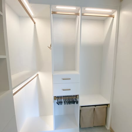White and gold walk in closet with lighting, double hang, laundry hampers, and pant rack.