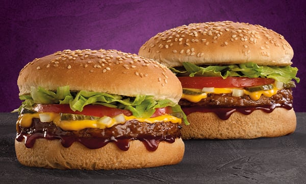 Two Wacky Wednesday beef burgers on an orange surface and a purple background.