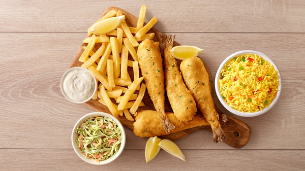 Four baby hakes with chips on a wooden board placed next to a bowl of rice, coleslaw and sauce.