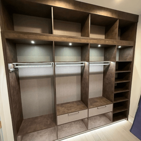 Primary closet in Maya Bronze with Corsican Weave backing and drawer faces, featuring suspended poles, graphite accessories, and integrated lighting for a sleek, modern storage solution.
