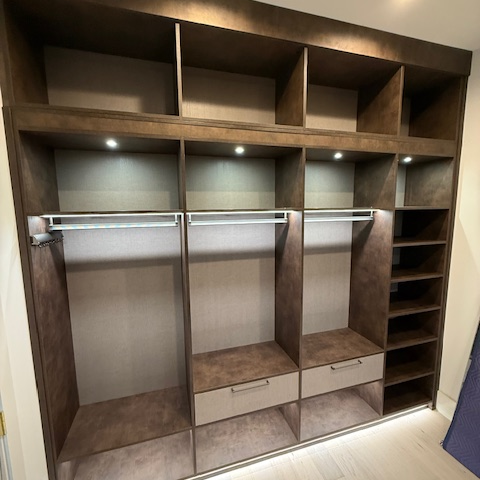 Primary closet in Maya Bronze with Corsican Weave backing and drawer faces, featuring suspended poles, graphite accessories, and integrated lighting for a sleek, modern storage solution.
