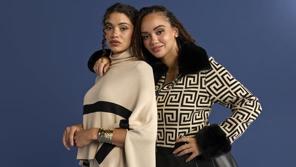 Two women are posing together in front of a blue wall.