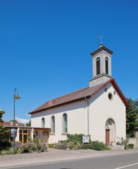 Außenansicht der Kirche vor blauem Himmel. Das Gebäude ist weiß gehalten während das Dach rot ist.