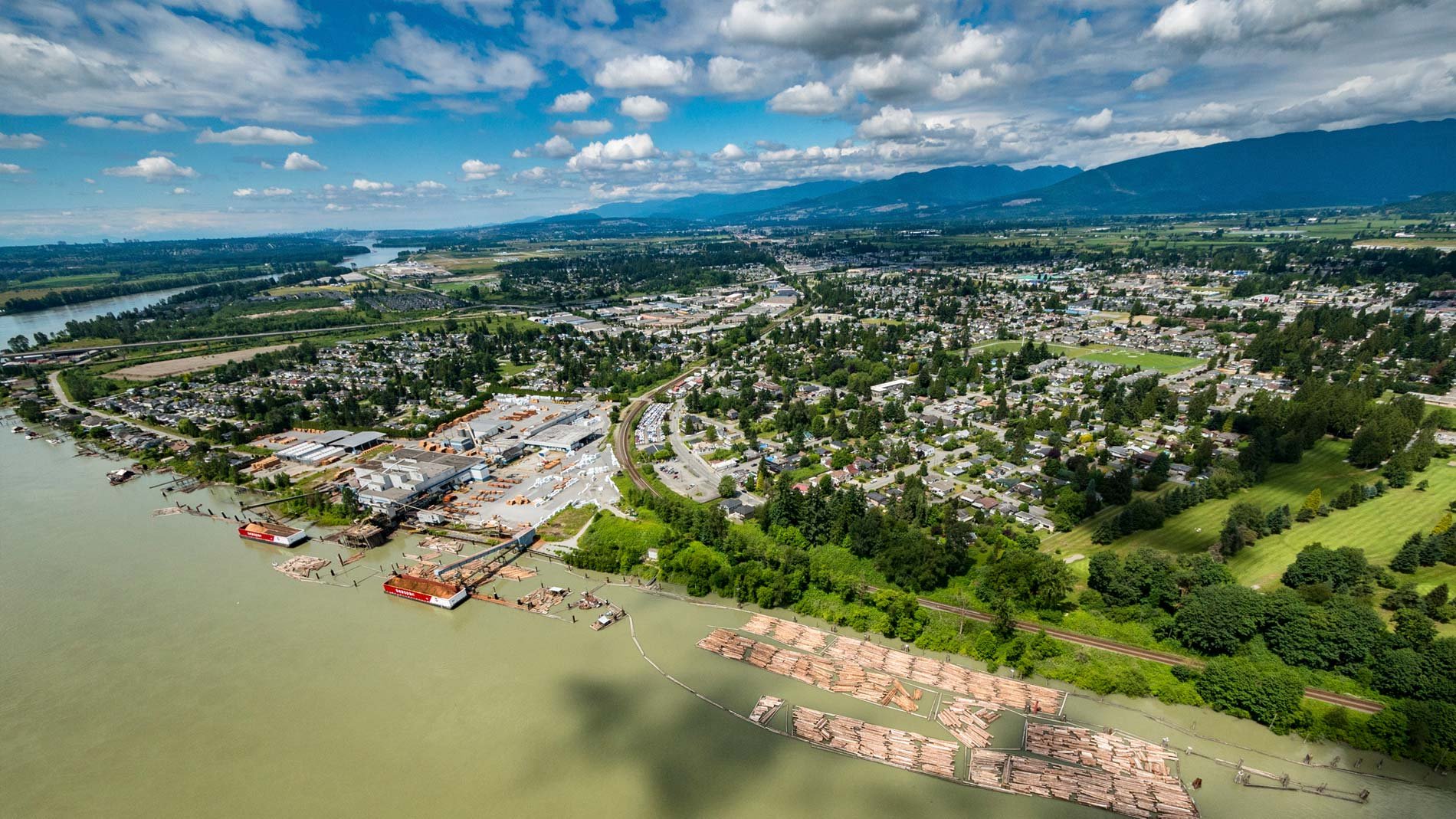 Aerial view of river along town of Maple Ridge, British Columbia, with mountain range in background.