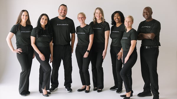 A group of Woodhouse Spa estheticians and massage therapists are standing together. Dressed in matching 'Masters of Mood Care' shirts, they embody the spa's commitment to wellness and professional development.