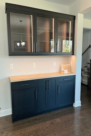 Custom cabinets with glass display shelving, integrated lighting, concealed storage, and wood countertops. This storage solution enhances home design while providing organized storage and refined home finishes.