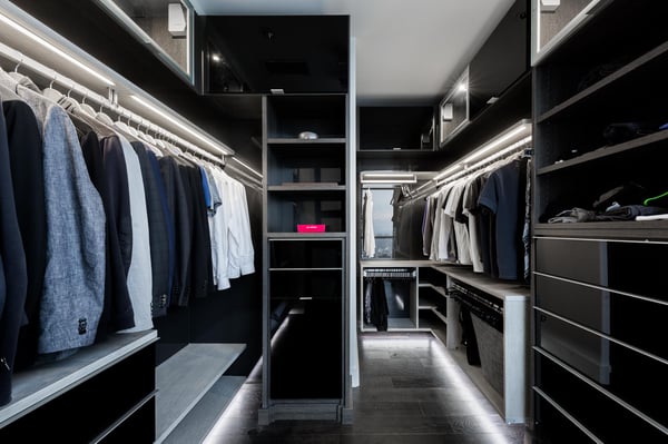Modern black and gray closet with one level of hanging, floating shelves, glossy drawer and door fronts, as well as toe kick lighting.