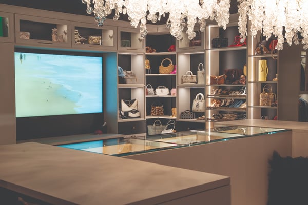 Luxury custom walk-in closet featuring LED-lit shelving, handbag and shoe storage, glass-front cabinets, and a central display island