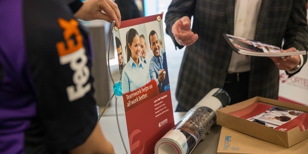 FedEx Office team member assisting a customer with printed marketing materials and posters at the counter.