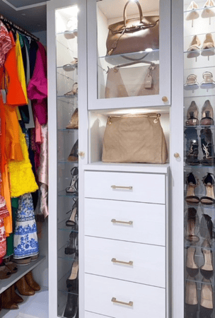 white luxury walk-in closet with drawers in the center and narrow shoe storage on either side with closed glass doors and glass shelving and hanging on either side modern gold hardware Westchester County New York