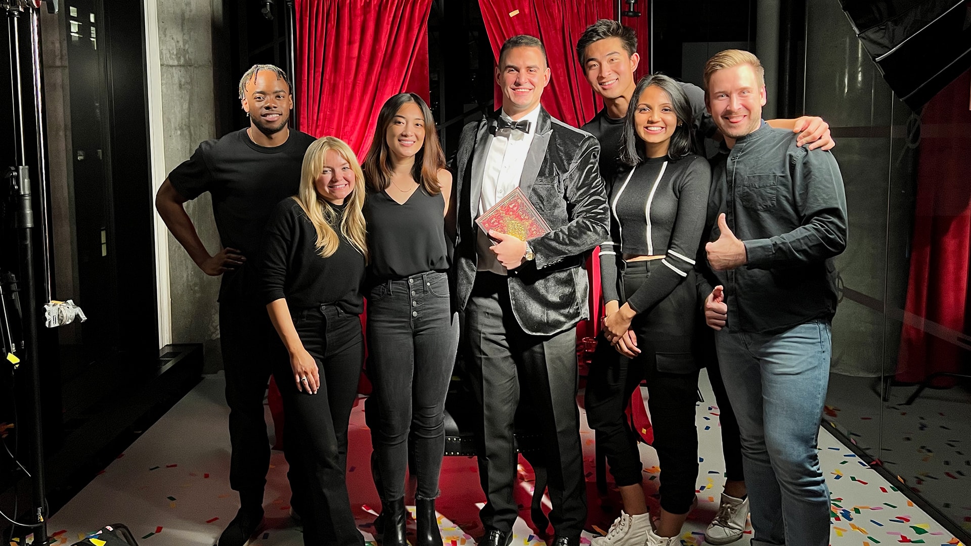 A group of Yext employees smiling for a photo with John Vatalaro in the middle wearing a suit for the Season of Search video
