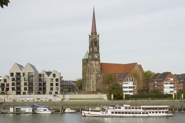 Ansicht des Kirchengebäudes am Weserufer mit einem Fährschiff.
