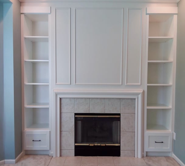 White built-in shelving units with central fireplace with a tiled surround and black glass insert, topped by decorative wall panel molding above the mantel in a home in Rochester, MI